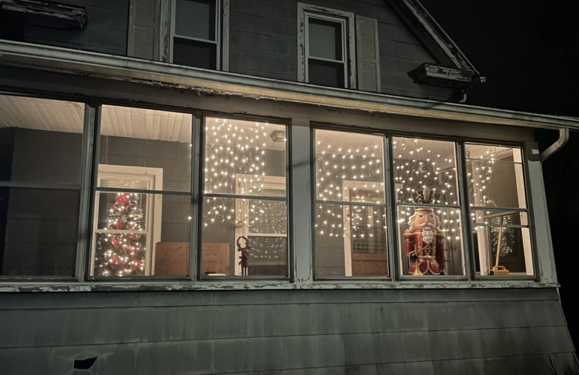Christmas lights hanging in windows of a house viewed from the outside. A large nutcracker is in one of the windows.